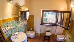 Une salle de bain avec un lavabo, deux toilettes, un miroir et une fenêtre.