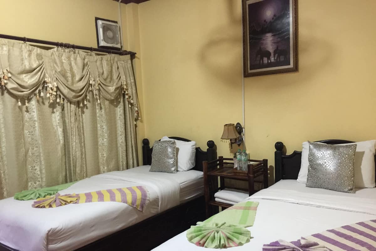 A hotel room with two single beds, a small table with bottles, a lamp, and a painting on the wall.