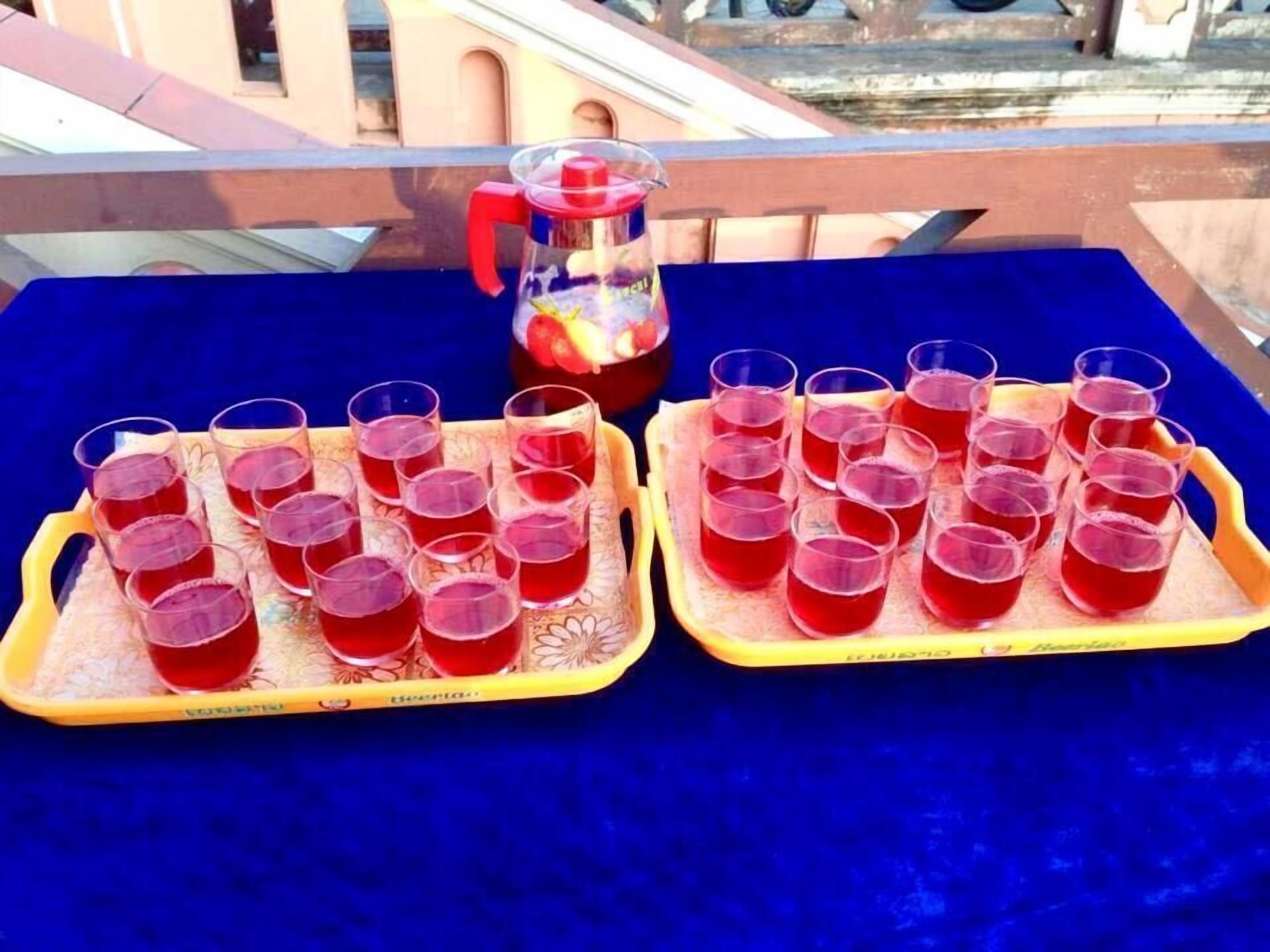 Two trays of red drinks on a blue tablecloth with a pitcher in the background.