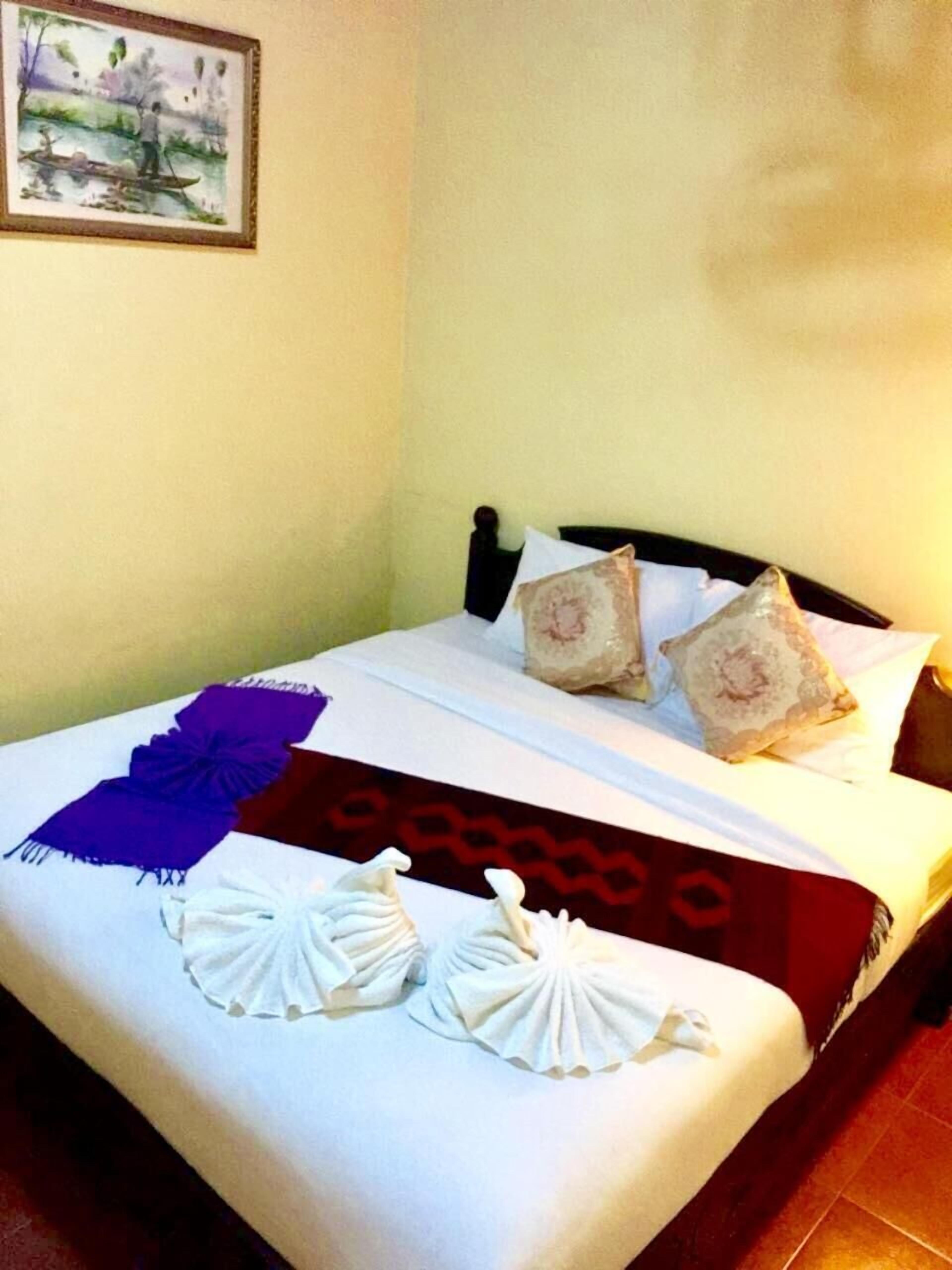 Una cama bien hecha con una colcha blanca y roja, dos almohadones decorativos y un cuadro en la pared.