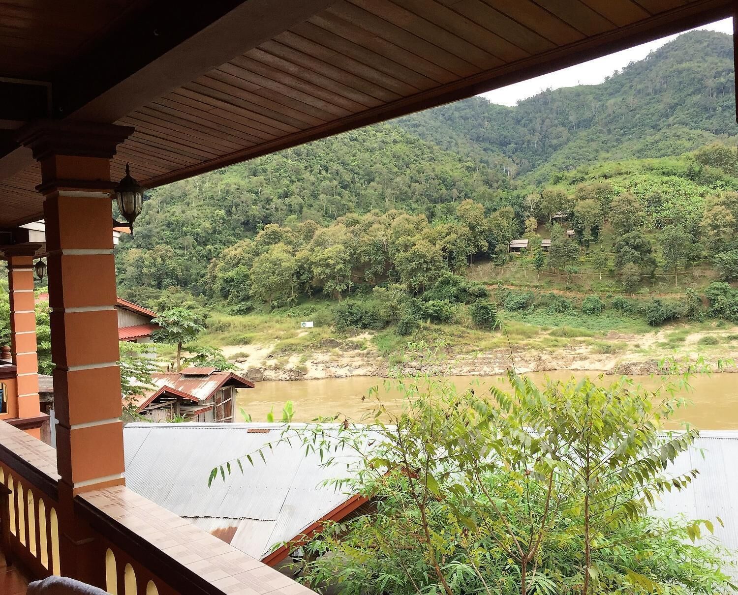 Vista de uma varanda coberta com vista para um rio e uma encosta arborizada.