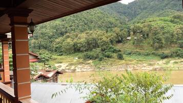 Vista de uma varanda coberta com vista para um rio e uma encosta arborizada.