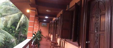 A covered corridor with wooden ceiling and walls, potted plants, and wooden doors.