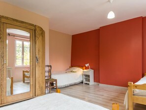 A bedroom with a wooden wardrobe, a bed, a chair, a nightstand, and a mirror.