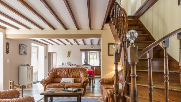 Ein geräumiges Wohnzimmer mit einer Holztreppe, Ledersofas und einem Essbereich im Hintergrund.