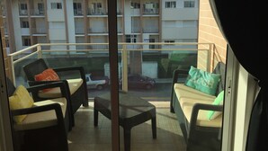 Uma varanda com mobiliário de vime, vista de um edifício residencial e um carro estacionado na rua.