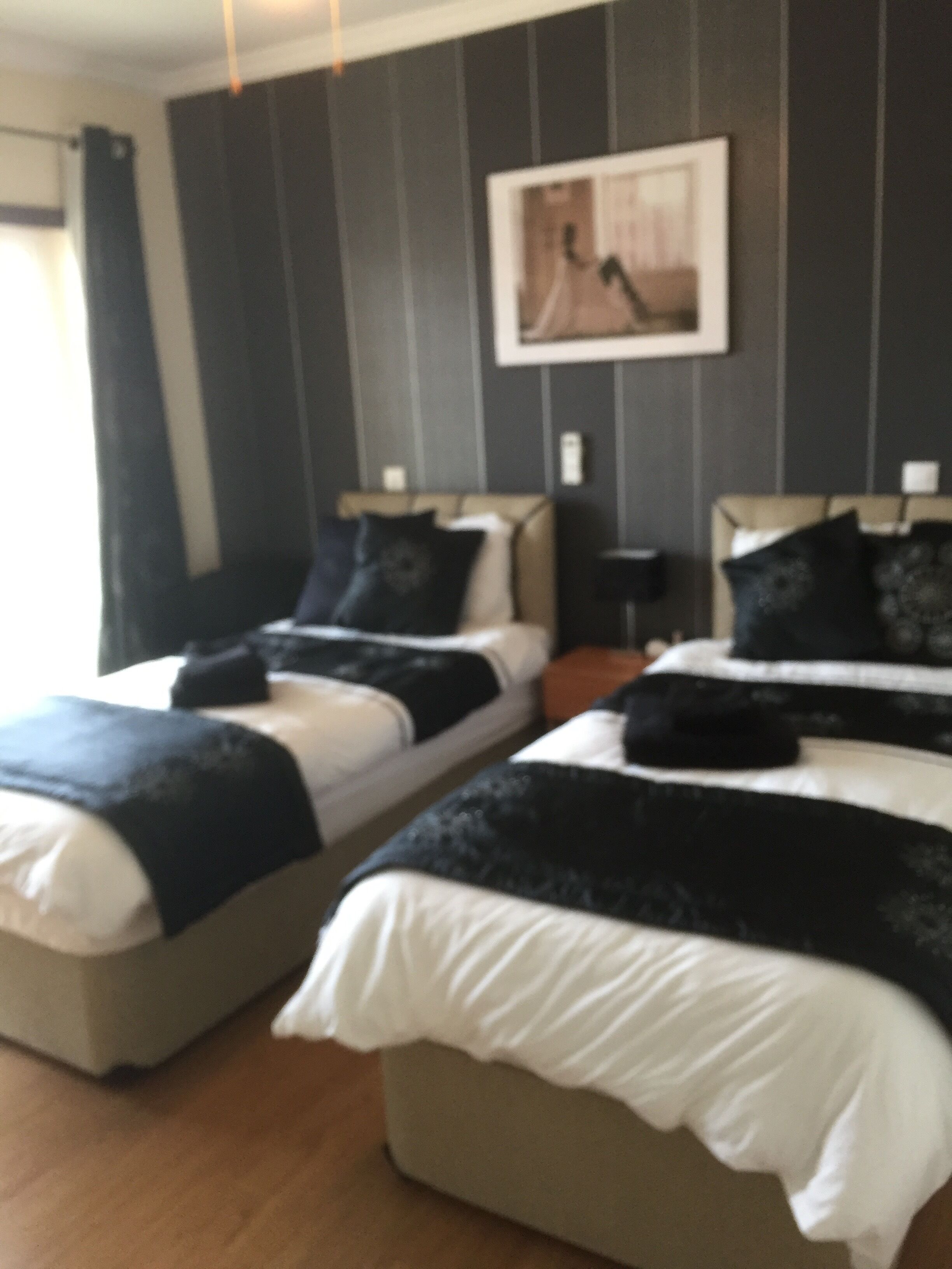 Ein Hotelzimmer mit zwei Betten, einem Bild an der Wand und einem Fenster mit Vorhängen.