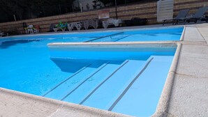 Piscina com borda azul, rodeada por um deck revestido de azulejos.