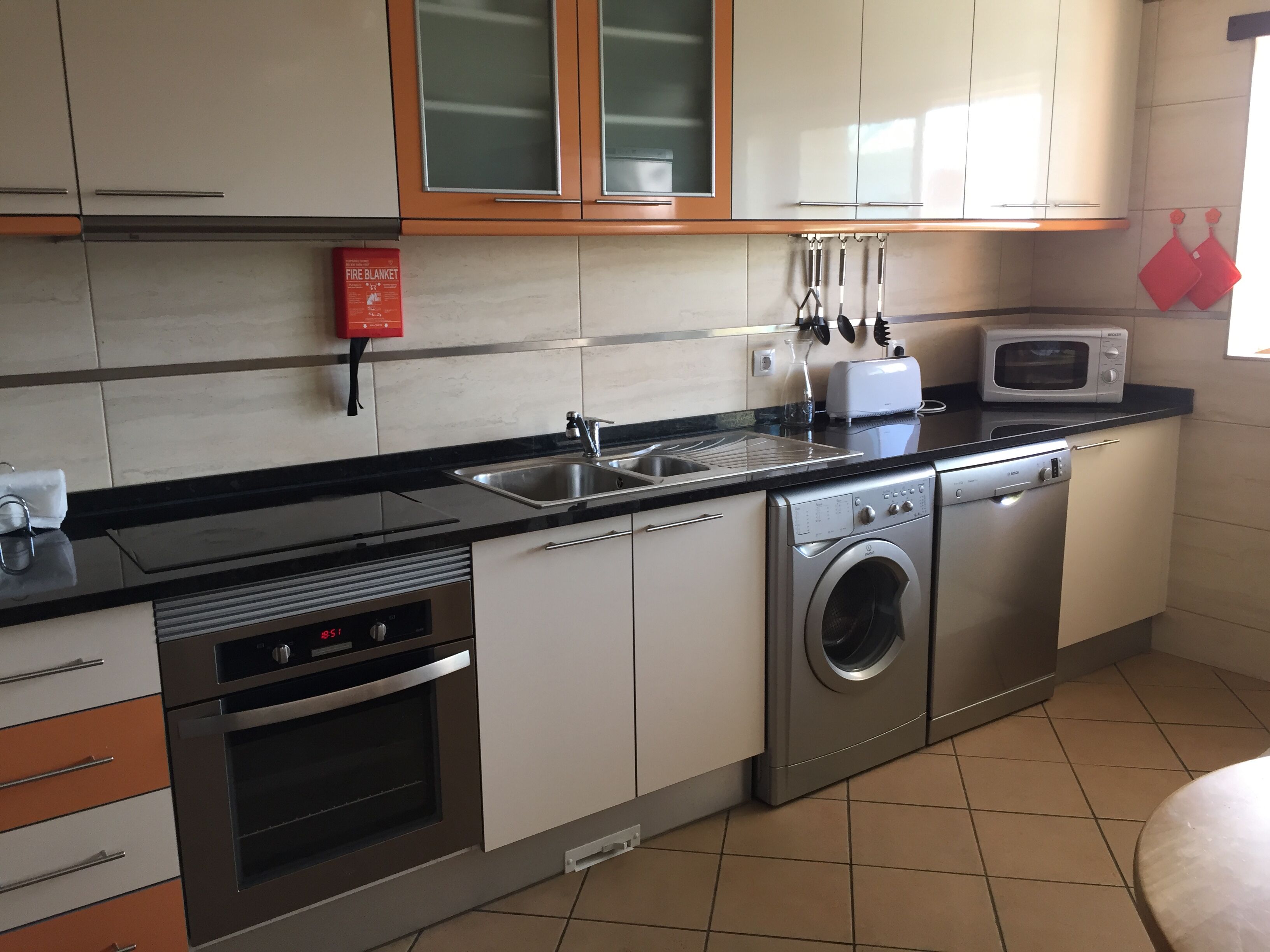 A modern kitchen with stainless steel appliances, a dishwasher, a microwave, and a fire blanket on the wall.