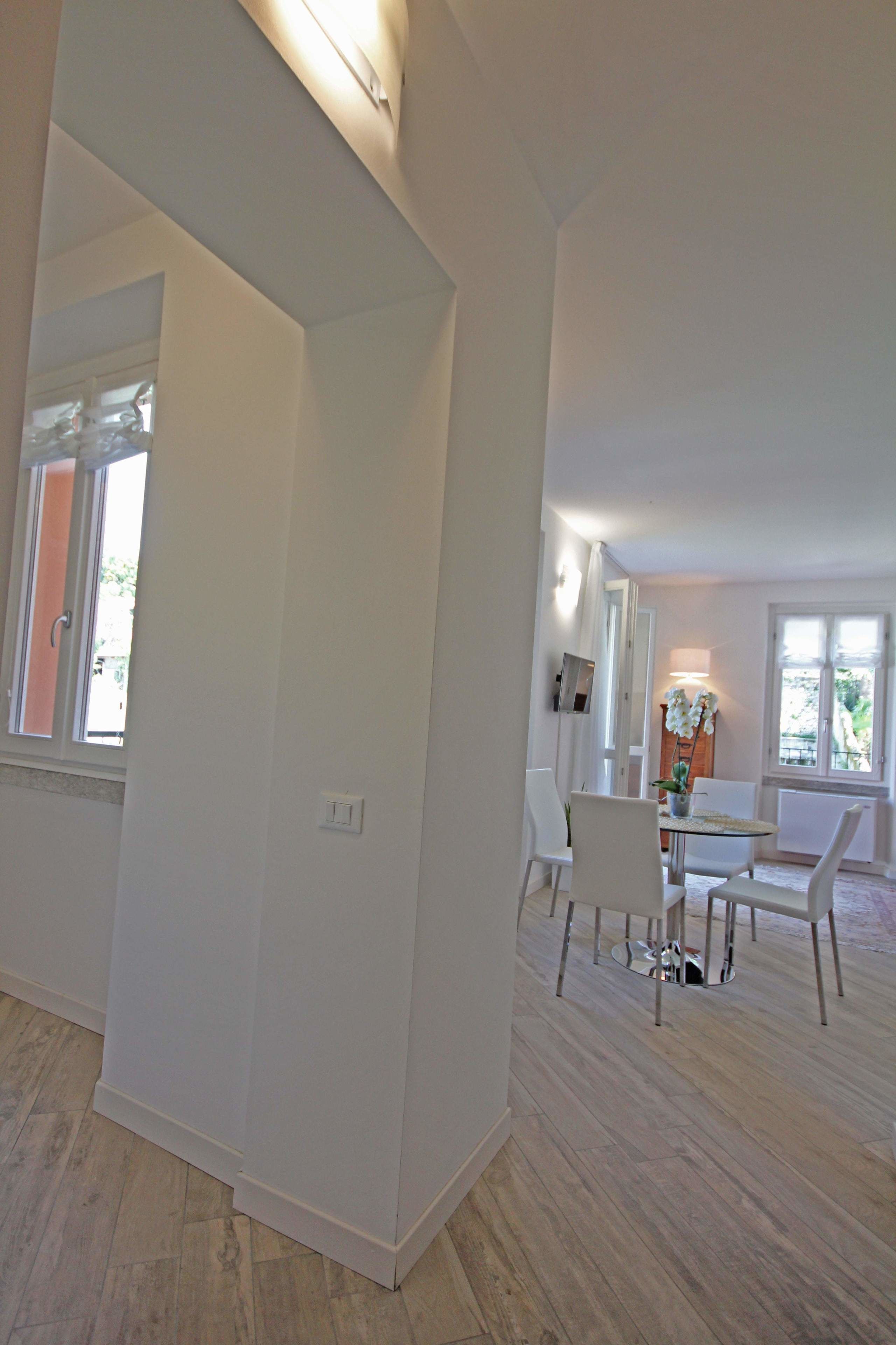 A spacious room with a large mirror, a dining area with a table and chairs, and a view of the outdoors through a window.
