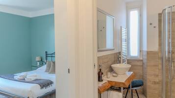 Une chambre à coucher comprenant un lit, une table de chevet et une commode. La salle de bain est équipée d’un lavabo, d’un miroir et d’une douche.