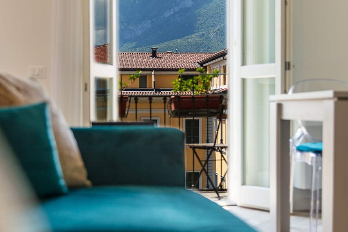 Una sala de estar con un sofá color turquesa, un ventanal de vidrio que da a una terraza exterior con vista a la montaña.