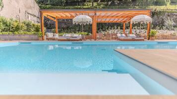 A pool area with a wooden pergola and lounge chairs.