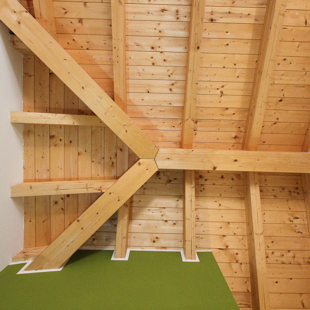 Estructura de techo de madera con vigas visibles y un suelo verde.