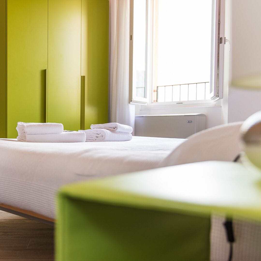 Ein Hotelzimmer mit Bett, grünen Wänden und einem Fenster mit Jalousien.