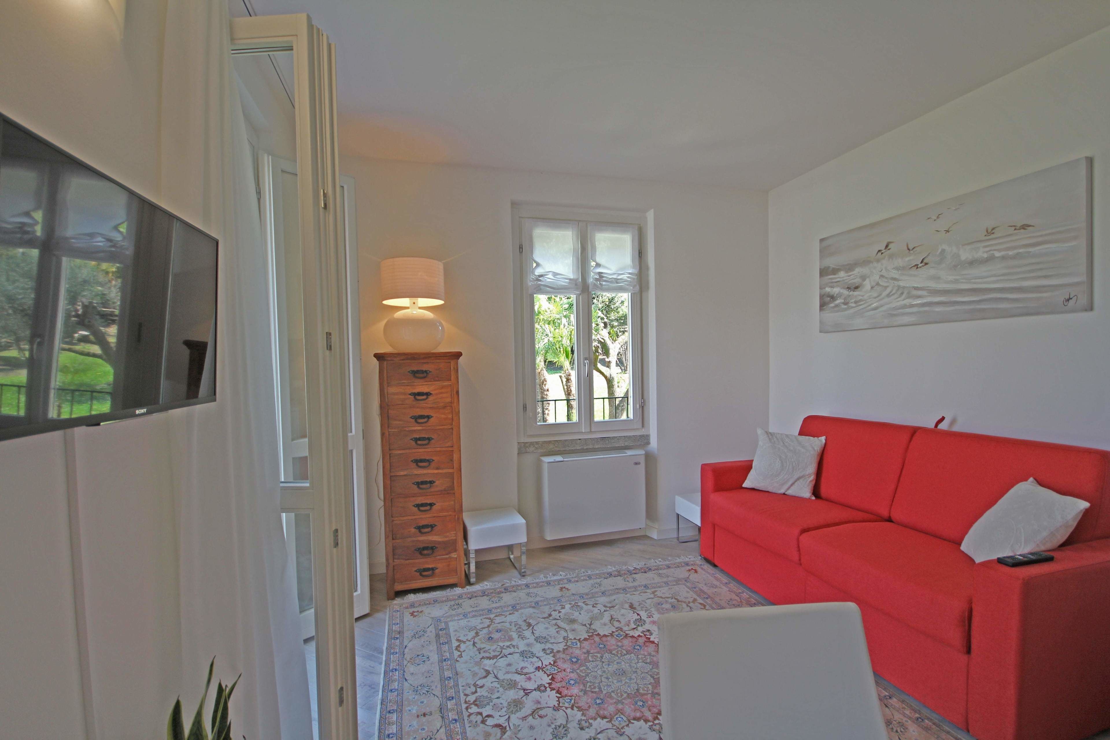 A living room with a red sofa, a wooden cabinet, a lamp, a radiator, and a painting on the wall.