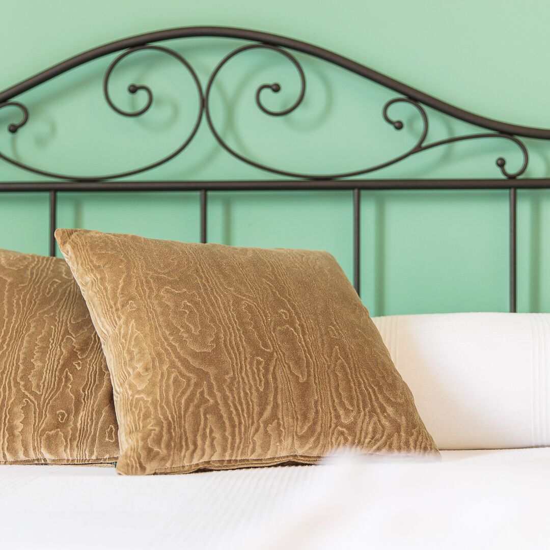 Un lit avec deux oreillers et une tête de lit en métal, adossé à un mur de couleur turquoise.