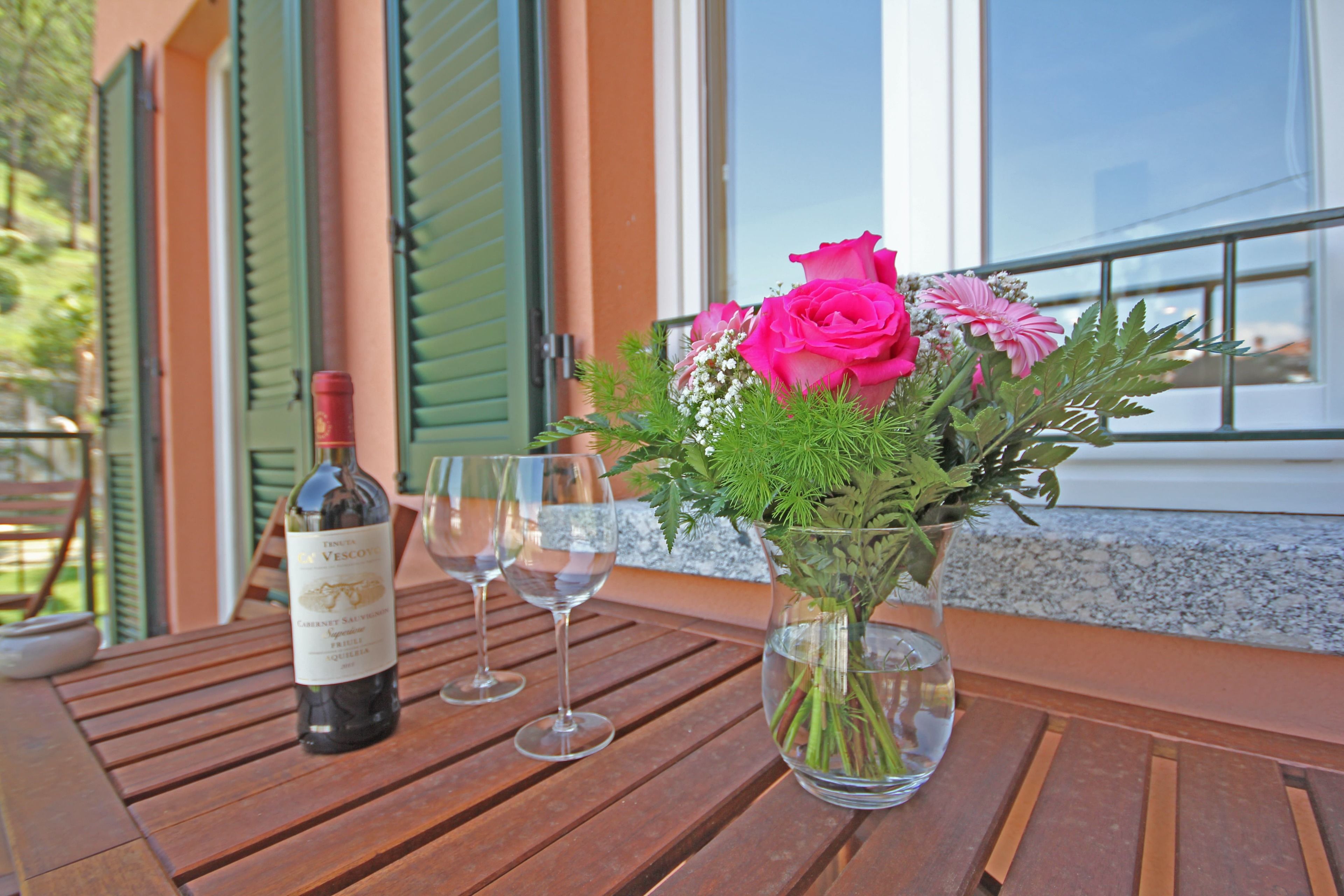 A wooden table with a bottle of wine, two glasses, and a vase with flowers.