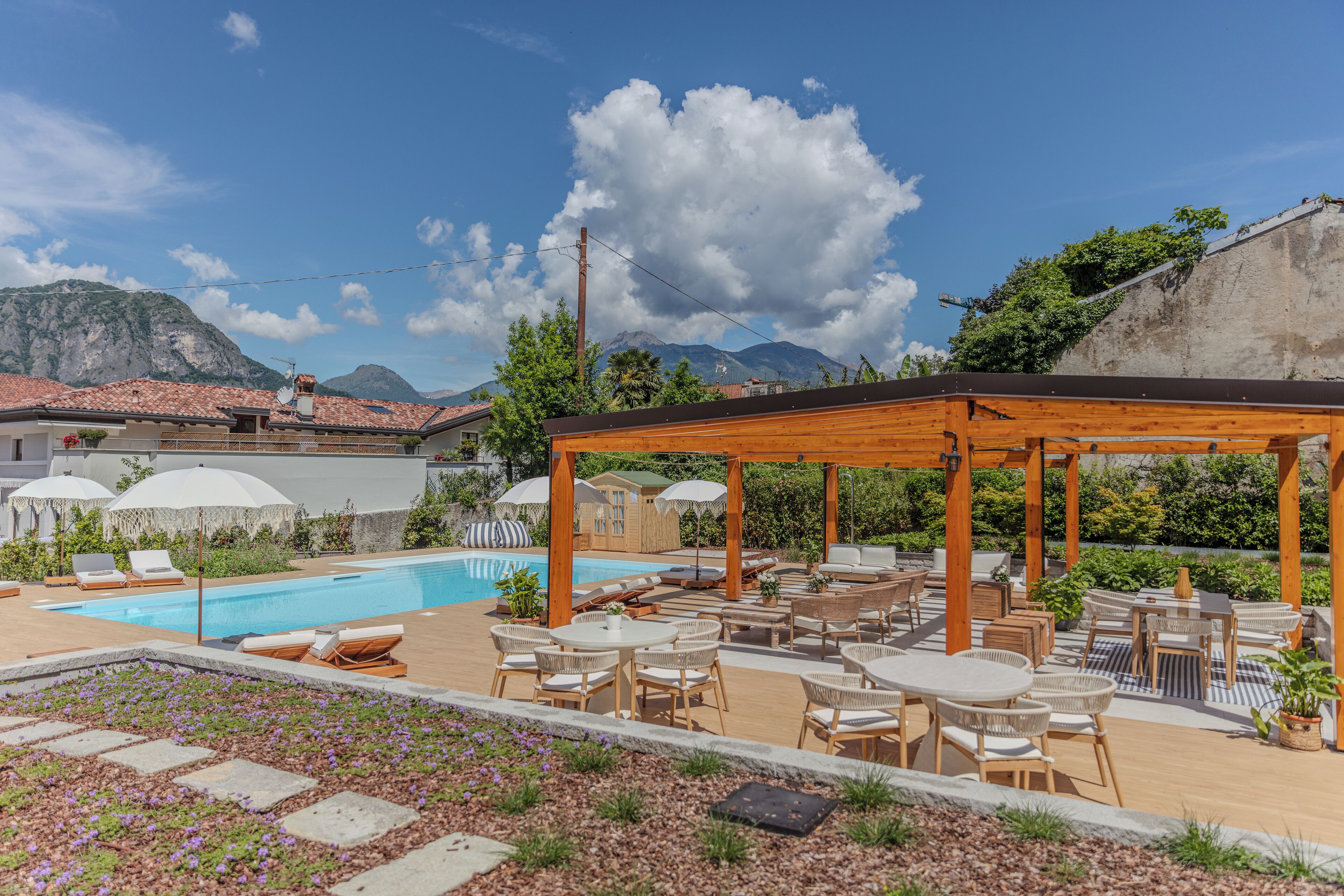 Ein Poolbereich mit Liegestühlen und Tischen, einer Holzpergola und Blick auf Berge.