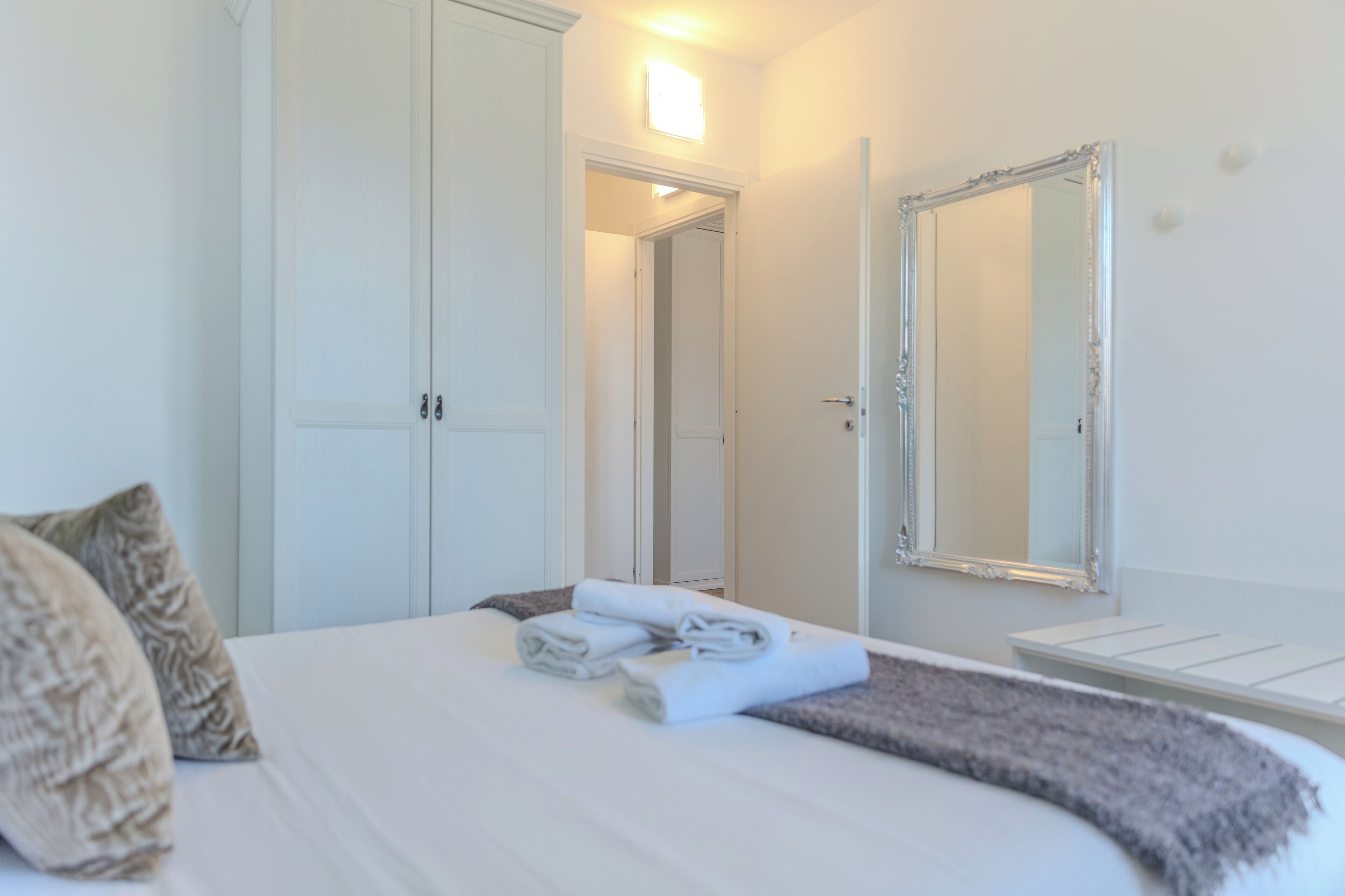 Una habitación de hotel con una cama, un espejo grande, un armario y una puerta que da a otra habitación.