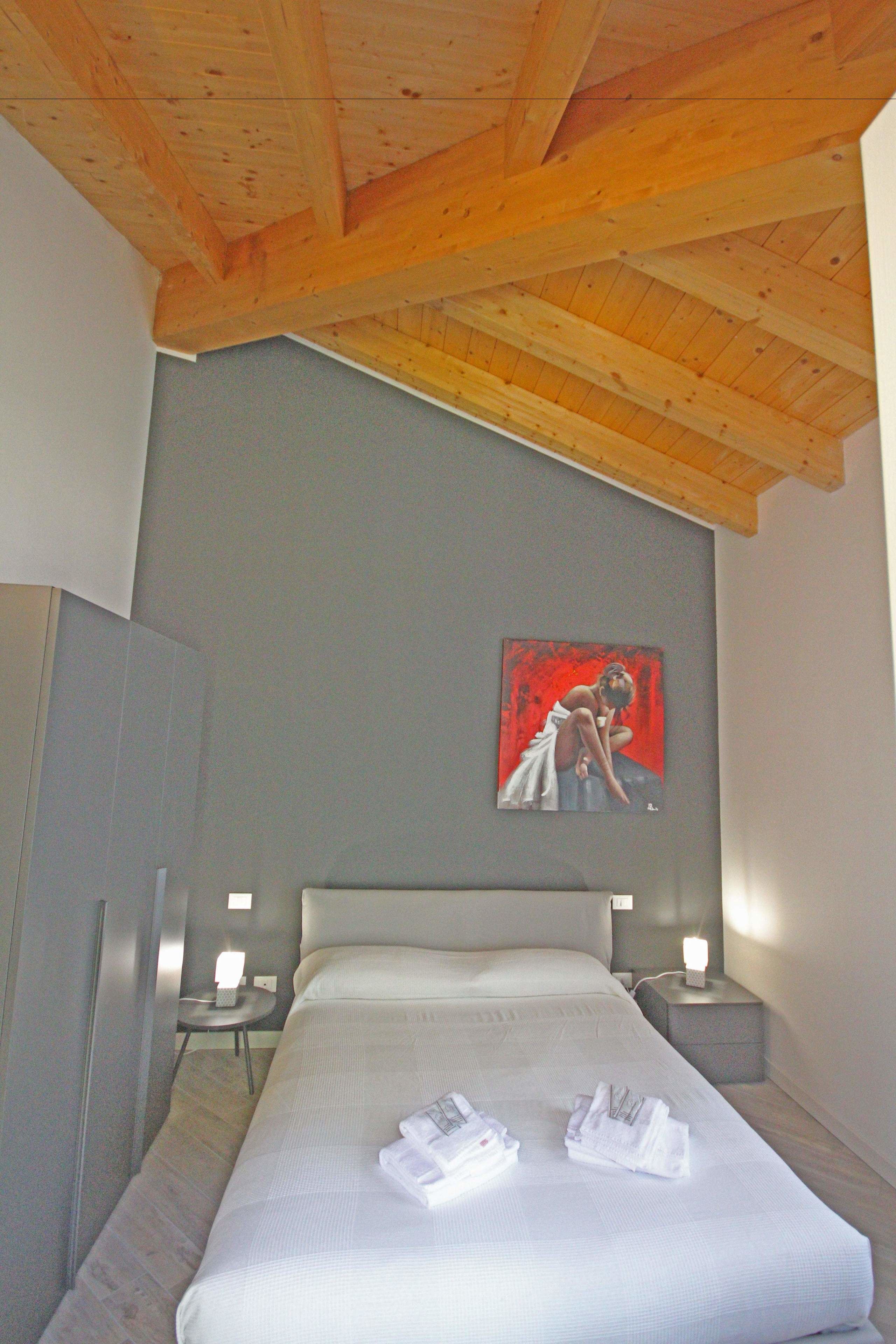 A hotel room with a large bed, wooden ceiling beams, a painting on the wall, and bedside lamps.