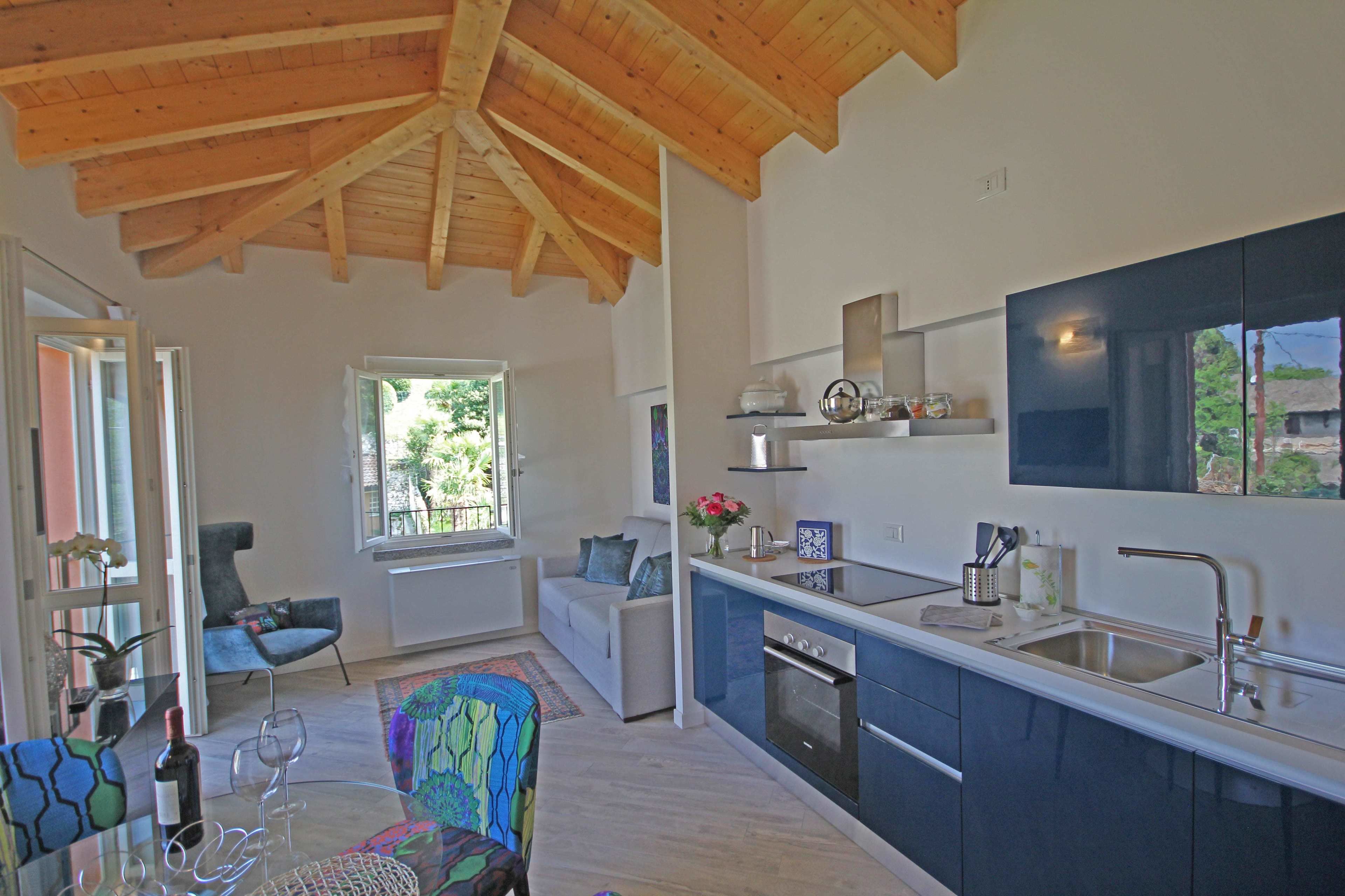 A modern kitchen with a wooden ceiling, a dining area with a glass table, and a view of greenery outside.