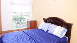 A bedroom with a bed, a window with blinds, a wooden nightstand, and a wall-mounted light fixture. - Hayuelos  Apartamentos Cerca al Aeropuerto el Dorado (Bogotá)
