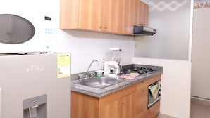 A compact kitchen with a microwave, stove, sink, and wooden cabinets. - Hayuelos  Apartamentos Cerca al Aeropuerto el Dorado (Bogotá)