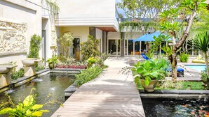 A courtyard with a wooden walkway, a small pond with koi fish, and various potted plants. - Villa La Luvier (Canggu)
