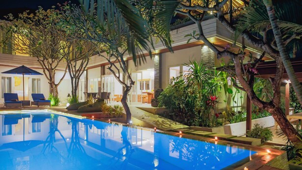 A swimming pool with lounge chairs and a well-lit patio area surrounded by tropical plants and trees. - Villa La Luvier (Canggu)