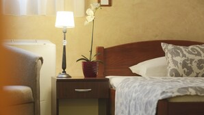 A hotel room with a bed, a nightstand with a lamp, a potted plant, and a chair. - Guesthouse Tara (Belgrade)