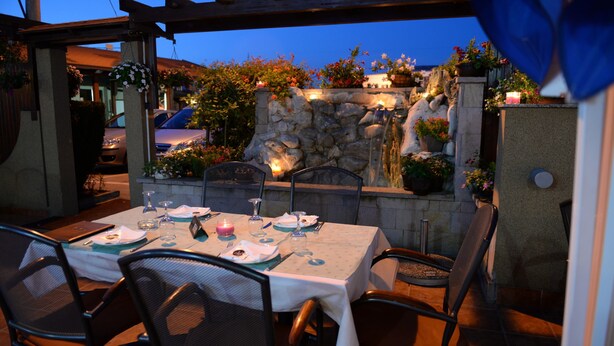 An outdoor dining area with a stone wall, waterfall feature, and potted plants. - Guesthouse Tara (Belgrade)