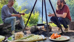 Two people sitting outdoors near a campfire with food and cooking utensils. - Kroppefjäll Bed & Breakfast (Dals Rostock)