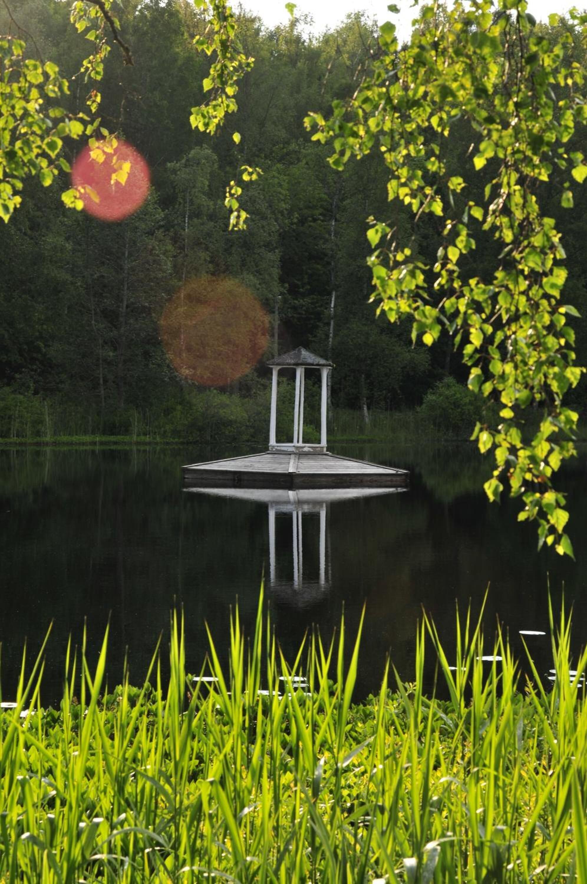 A gazebo on a calm lake surrounded by lush greenery.