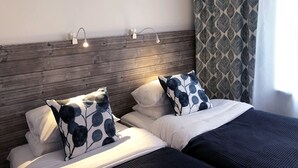 A double bed with white and dark blue bedding, two wall-mounted reading lights, and a patterned curtain. - Kroppefjäll Bed & Breakfast (Dals Rostock)