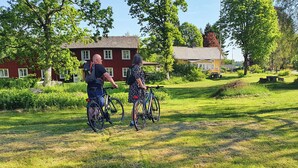 Two people on bicycles in a grassy area with houses in the background. - Kroppefjäll Bed & Breakfast (Dals Rostock)