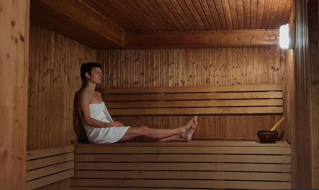Eine Person sitzt in einer Holzsauna mit einer Rippenbank und einer kleinen Schale mit einem Stock.
