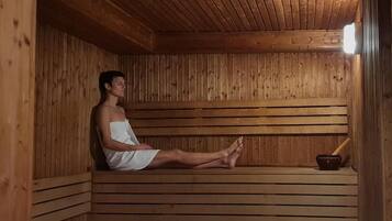 Eine Person sitzt in einer Holzsauna mit einer Rippenbank und einer kleinen Schale mit einem Stock.