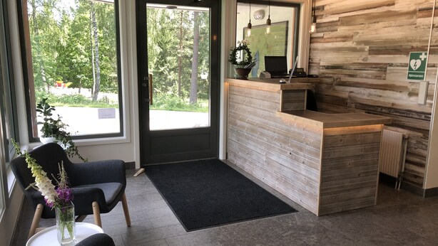 A reception area with a wooden reception desk, a black door, and a view of trees outside. - Kroppefjäll Bed & Breakfast (Dals Rostock)
