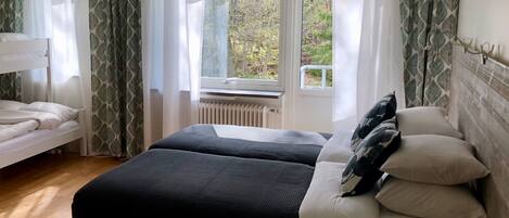 A bedroom with a bunk bed, a single bed, and a window with a view of trees.