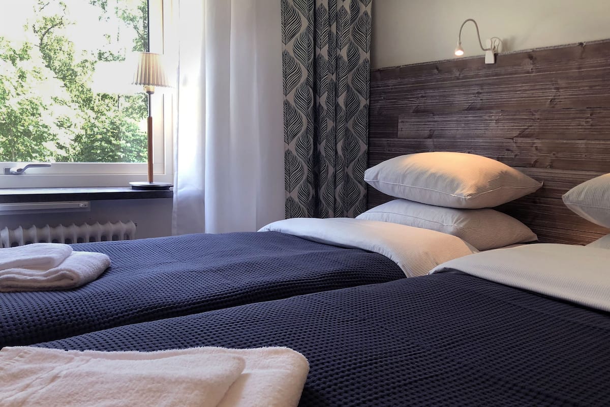 A hotel room with two beds, a window with curtains, a radiator, and a wooden headboard.