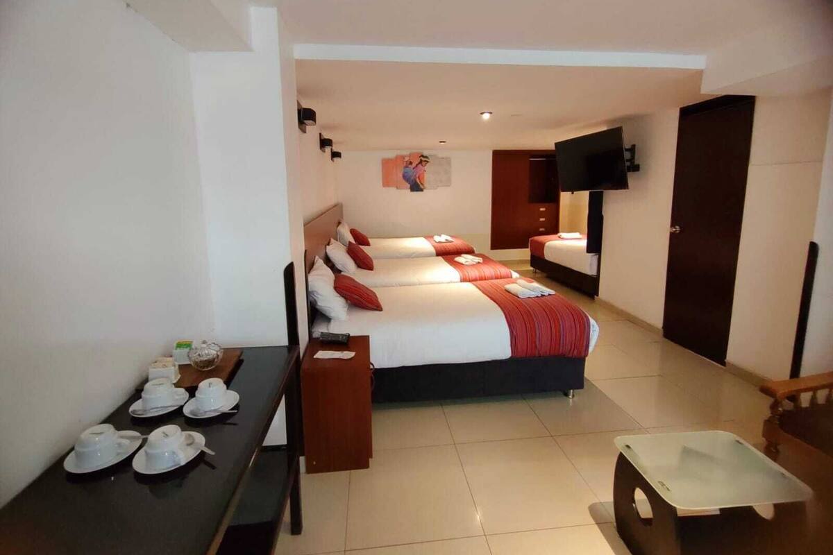 A hotel room with two beds, a desk with tea sets, a flat-screen TV, and a wooden wardrobe.