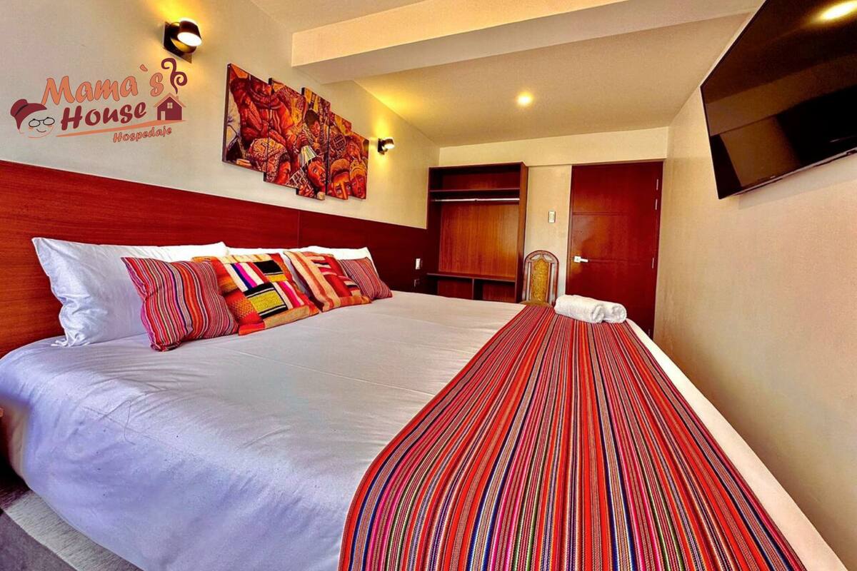 A hotel room with a large bed, a wall-mounted TV, and a painting above the bed.