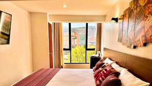 A hotel room with a large bed, a view of the cityscape, and a painting on the wall. - Mama's House (Cusco)