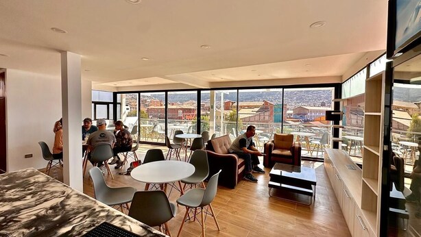 A modern interior with a large window, a dining area, and a seating space with a view. - Mama's House (Cusco)