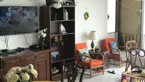 Een woonkamer met een televisie, houten meubels, een eettafel met bloemen en een balkon met stoelen.