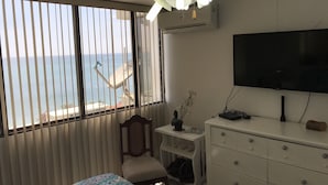 Een hotelkamer met een bed, bureau, stoel, dressoir, televisie en uitzicht op zee.