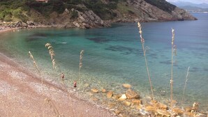 Un paysage côtier caractérisé par une eau turquoise et limpide, un rivage rocheux et une colline à la végétation clairsemée.