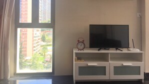 A living room with a flat-screen TV on a white TV stand, a small clock, and a shelf with a plant and a sign that reads "Beach". - SUPER VIEWS IN SUIT. NEW WITH FREE WIFI / PETS PERMITTED!(4 people) (Benidorm)