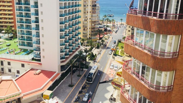 A high-rise hotel with multiple balconies, a street view with parked cars, and a beach in the background. - SUPER VIEWS IN SUIT. NEW WITH FREE WIFI / PETS PERMITTED!(4 people) (Benidorm)